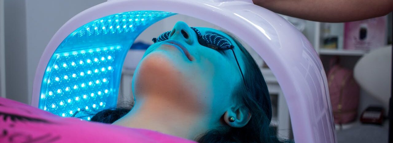 zipwp-image-4207236 Unrecognizable woman with dark hair with pierced ears lying under ultraviolet lamp while visiting contemporary clinic and spending time in modern salon